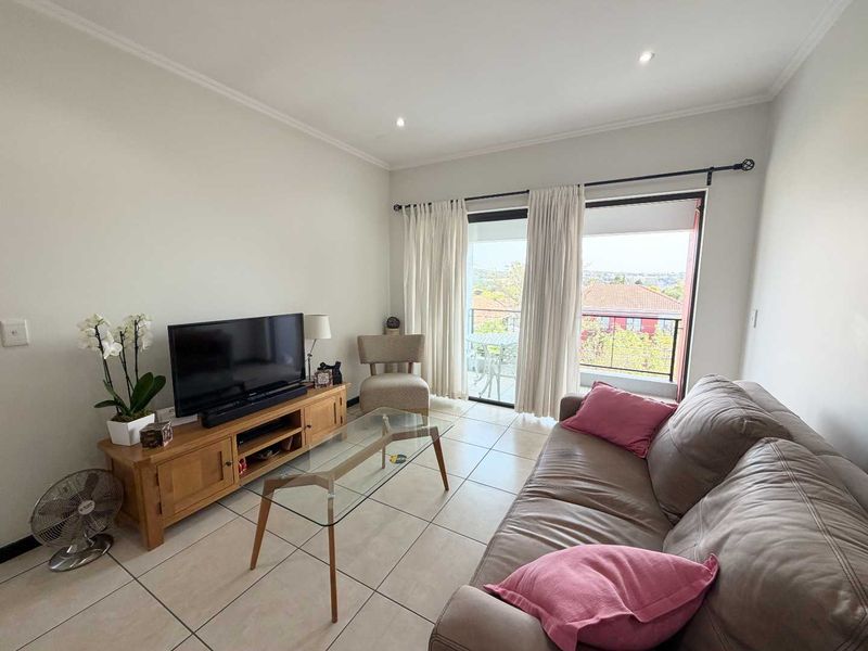 A bright living room featuring tiled flooring, recessed downlighting, and a sliding glass door providing access to a balcony with neighborhood views.