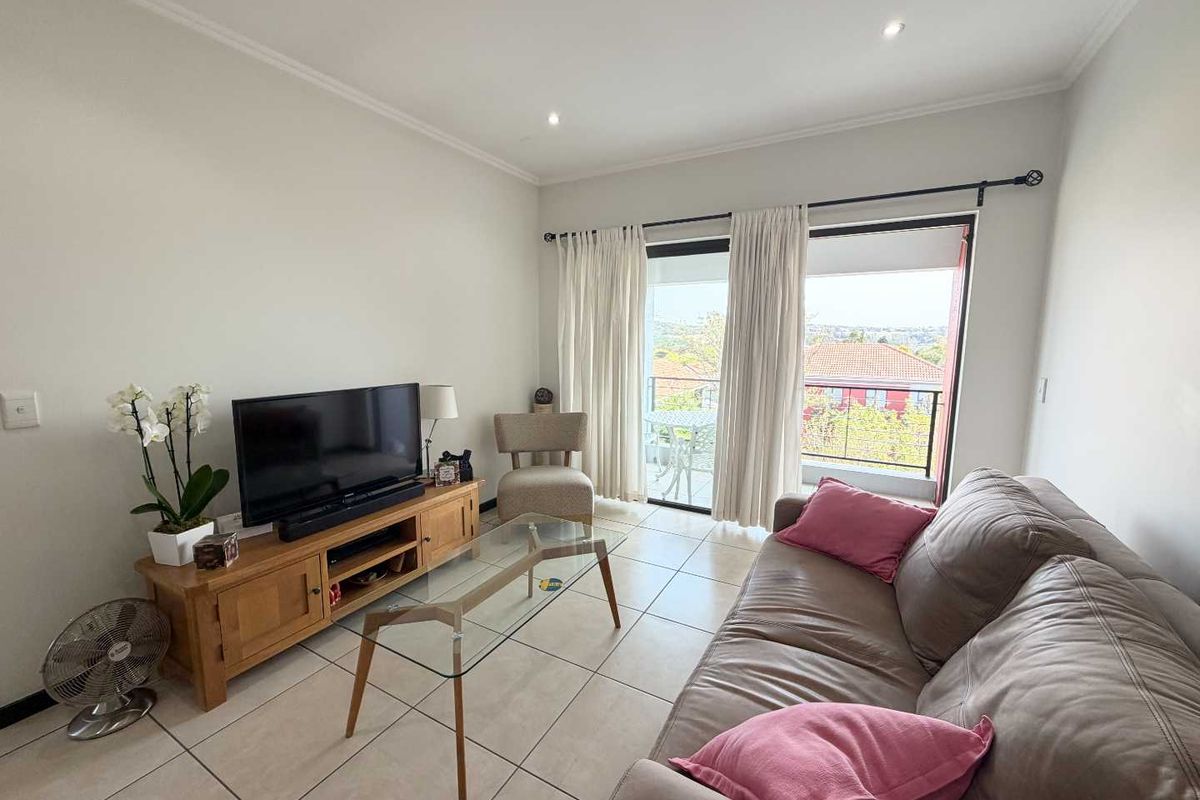 A bright living room featuring tiled flooring, recessed downlighting, and a sliding glass door providing access to a balcony with neighborhood views.
