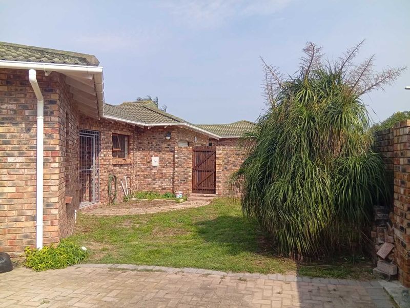 Rear exterior view of a face brick house featuring a paved area, lawn, and secure side access gate.