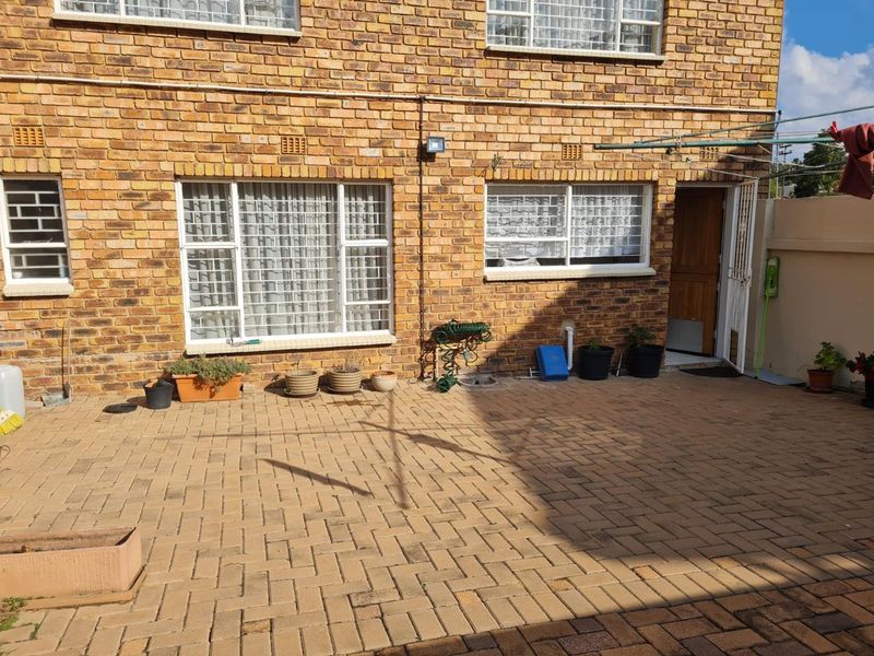 A paved rear courtyard area featuring a face brick facade, security-fitted windows, and a timber door, providing a functional outdoor space.