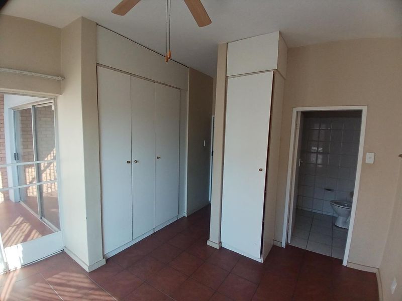 Spacious bedroom featuring built-in cupboards, tiled flooring, a ceiling fan, and direct access to an outdoor balcony area.