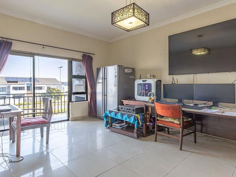 A spacious living area featuring tiled flooring, a large sliding glass door providing balcony access, and a central ceiling light fixture.