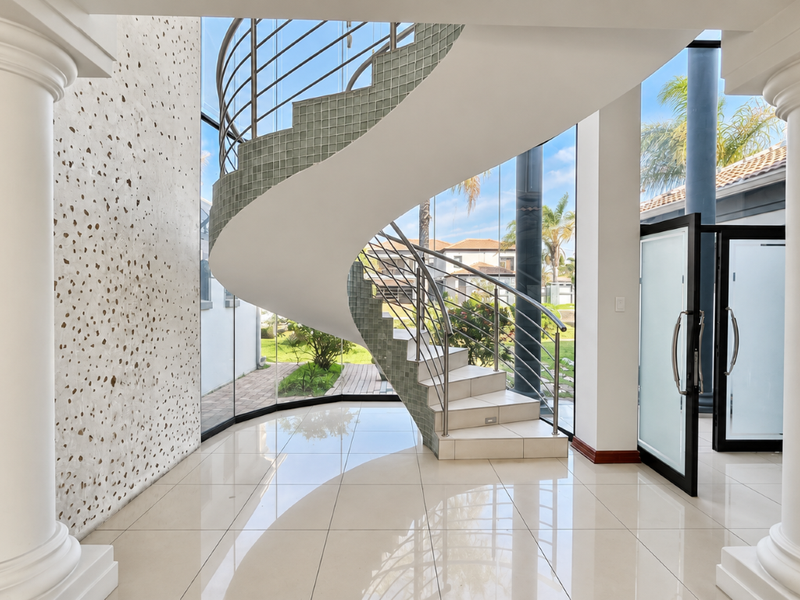 A grand entrance hall featuring a striking spiral staircase, polished tile flooring, and expansive floor-to-ceiling windows that provide abundant natural light.