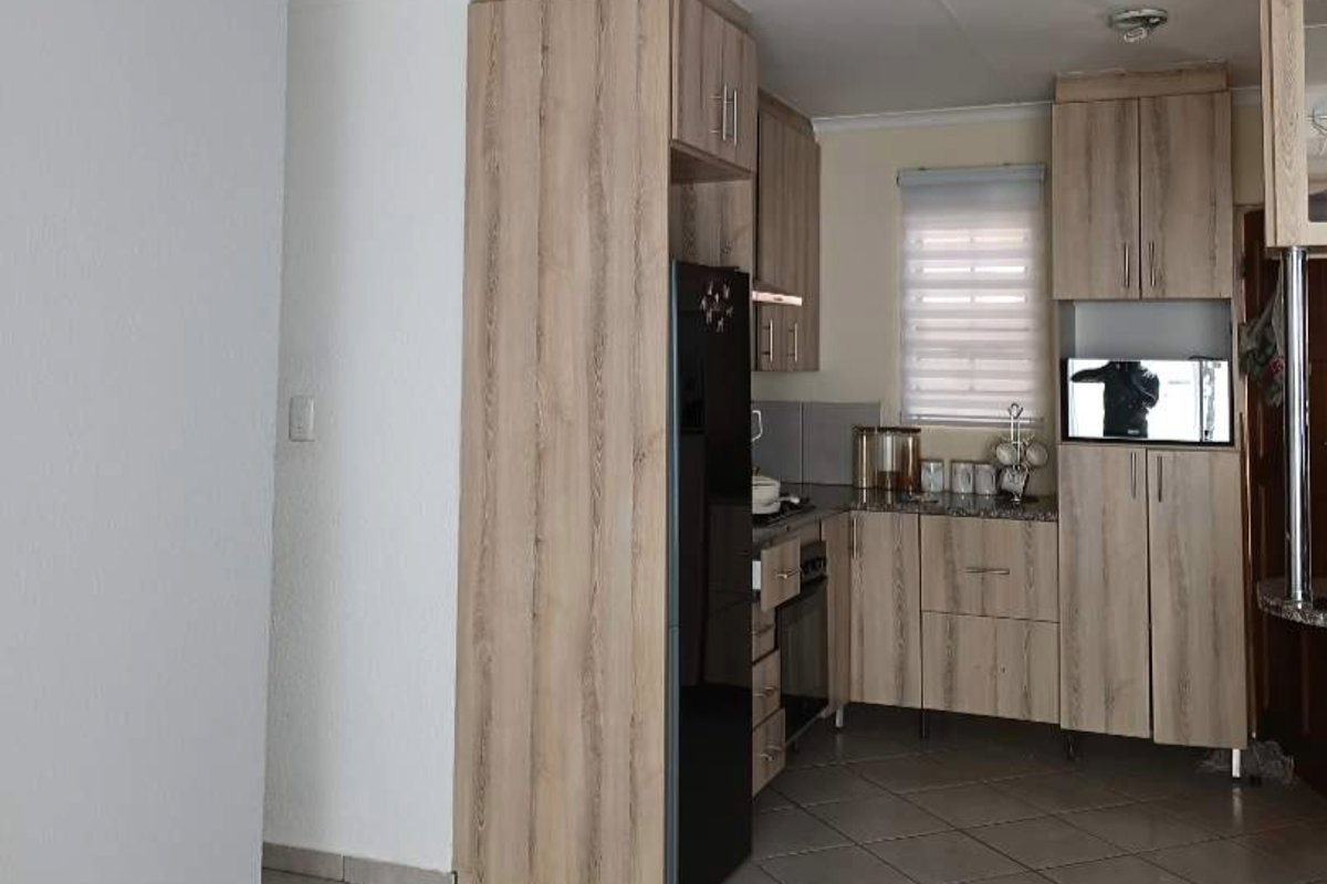 A functional kitchen featuring light wood-grain cabinetry, built-in appliances, and tiled flooring, offering a clean and practical workspace.