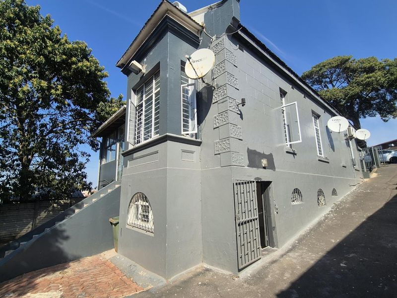 Rear exterior view of the property featuring grey painted walls, security bars on windows, satellite dishes, and an external staircase leading to the upper level.