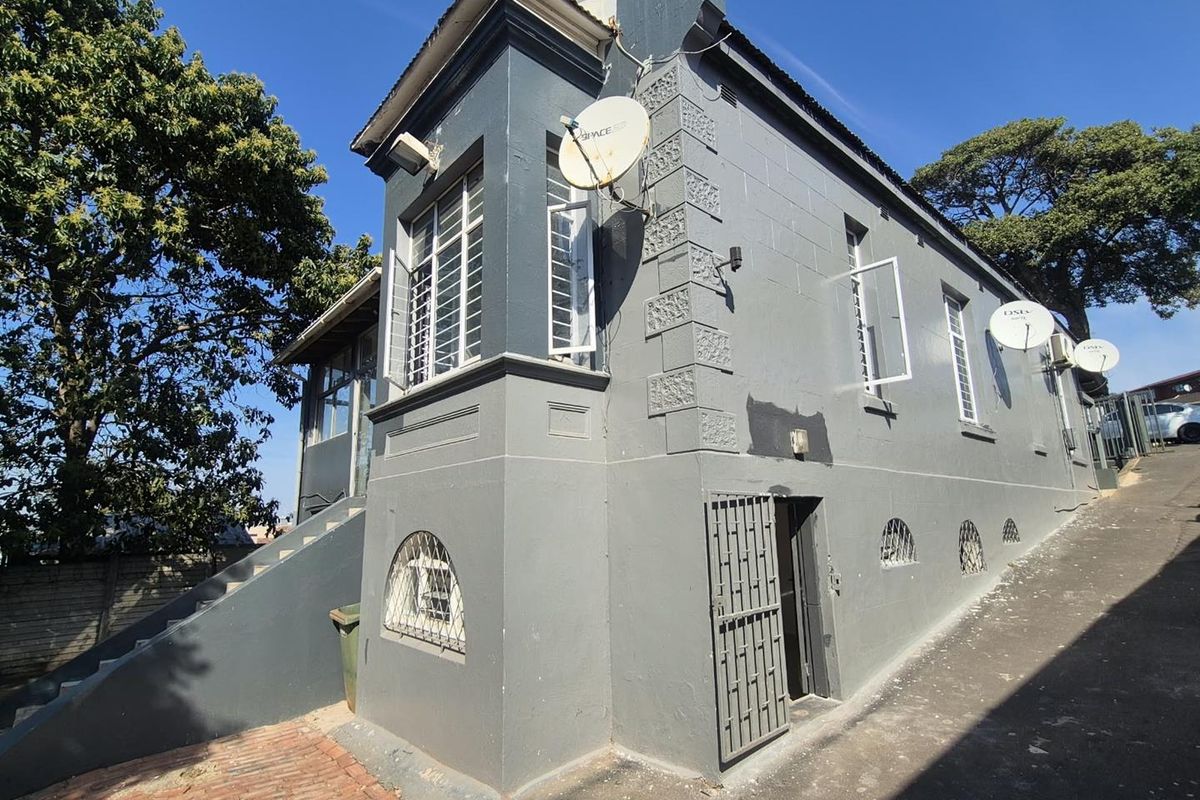 Rear exterior view of the property featuring grey painted walls, security bars on windows, satellite dishes, and an external staircase leading to the upper level.