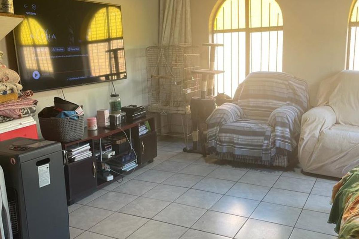A living room featuring tiled flooring, a timber ceiling, and arched windows with security bars, offering a dated but functional living space.