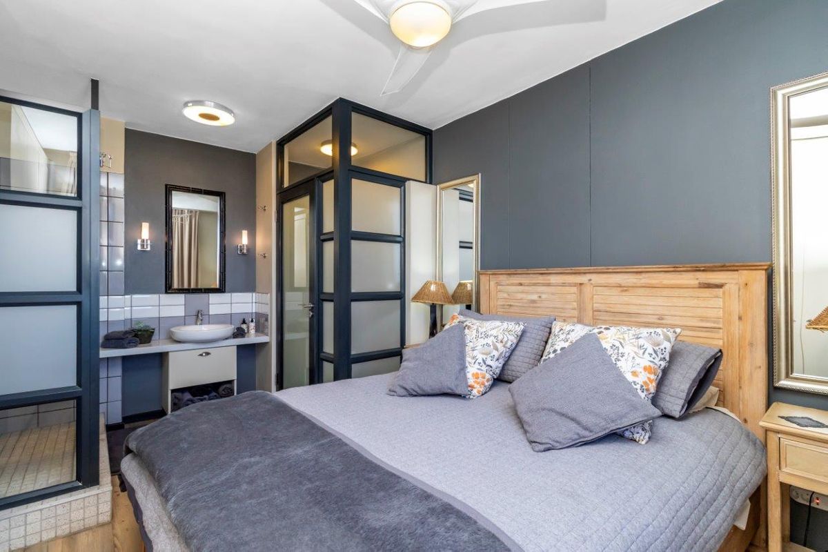 A modern bedroom featuring an integrated open-plan bathroom area with a vessel sink, vanity, and glass-partitioned shower enclosure.