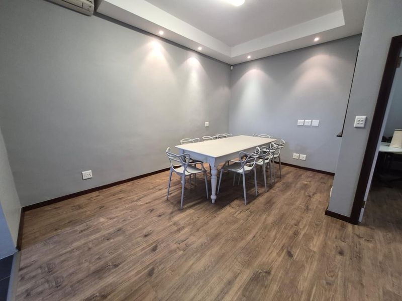 A modern office space featuring laminate wood flooring, recessed ceiling lighting, and a cove ceiling design, providing a clean and professional work environment.