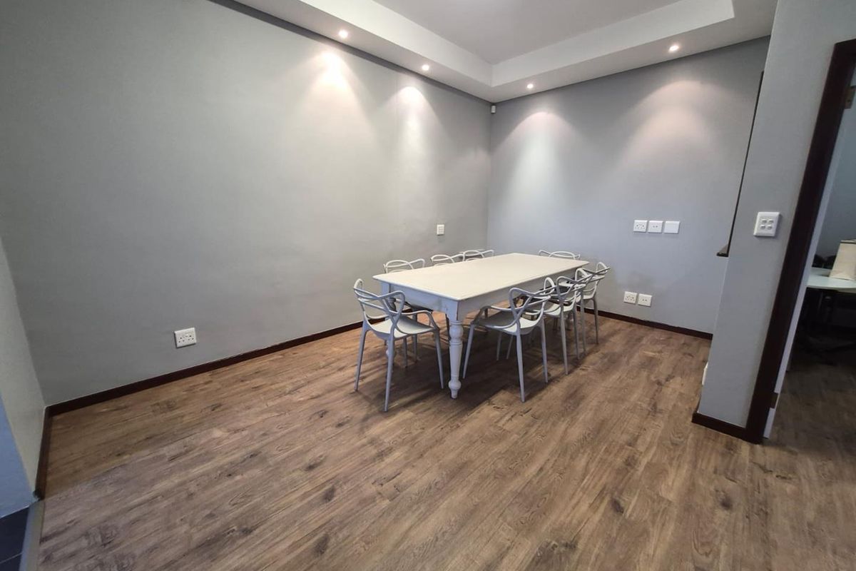 A modern office space featuring laminate wood flooring, recessed ceiling lighting, and a cove ceiling design, providing a clean and professional work environment.