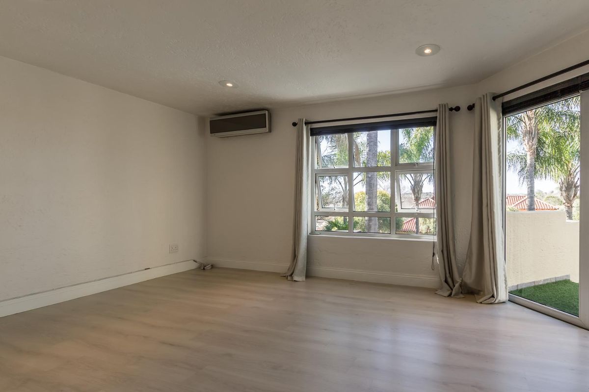 A bright, empty living room featuring light wood-look flooring, a wall-mounted air conditioning unit, and sliding glass doors leading to an outdoor balcony.