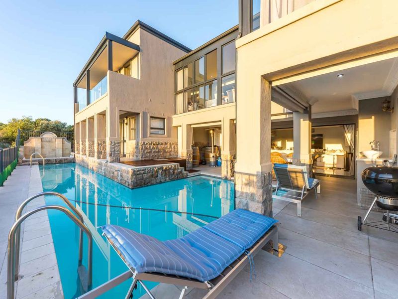A spacious outdoor entertainment area featuring a swimming pool, stone-clad architectural details, and a covered patio space seamlessly connected to the interior living area.