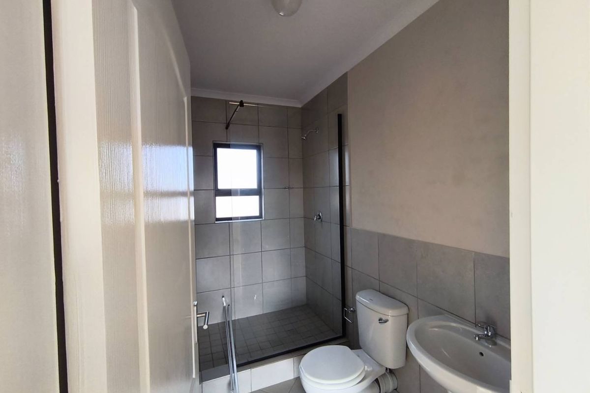 A functional bathroom featuring a walk-in shower with grey tiling, a pedestal basin, and a standard toilet.