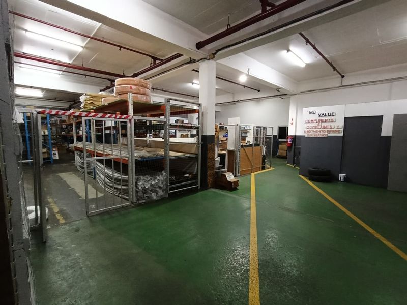 Industrial warehouse space featuring exposed fire sprinkler systems, durable painted concrete flooring, and integrated metal shelving units for storage.