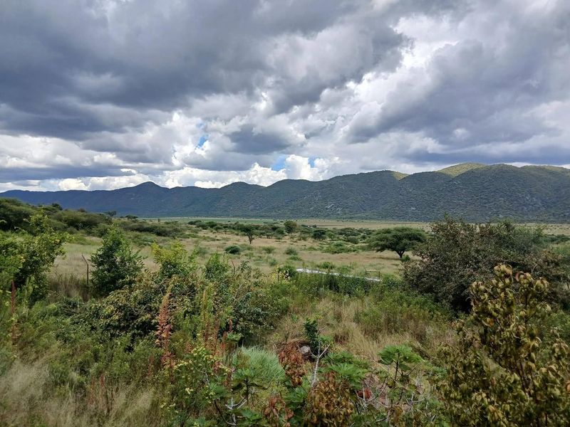 Expansive scenic view of the farm landscape featuring rolling hills and natural vegetation under a cloudy sky.