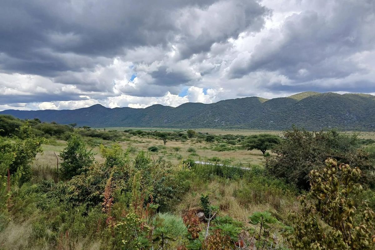 Expansive scenic view of the farm landscape featuring rolling hills and natural vegetation under a cloudy sky.