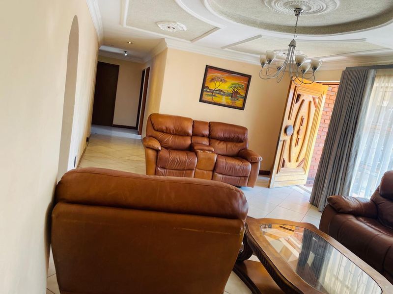 Spacious living room featuring ornate ceiling detailing, tiled flooring, and a solid wood entrance door leading to the exterior.