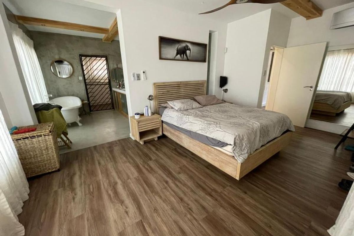 Spacious bedroom featuring wood-look flooring, exposed timber ceiling beams, and an open-plan en-suite bathroom with a freestanding bathtub.