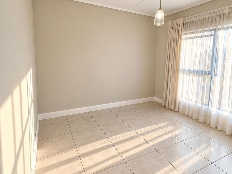 A bright and spacious empty bedroom featuring neutral tiled flooring, a modern pendant light, and large sliding glass doors with installed curtain tracks.