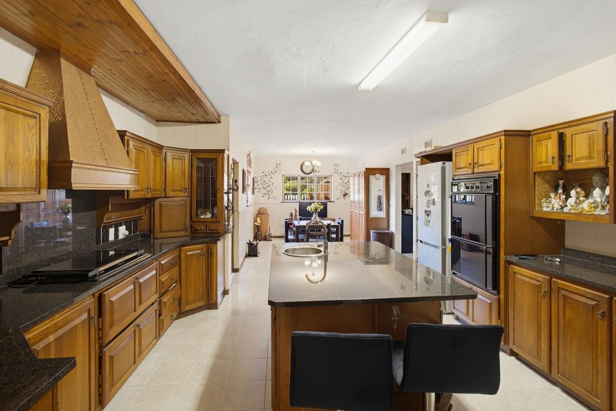 Spacious kitchen featuring extensive wooden cabinetry, granite countertops, a central island with a sink, and integrated appliances, offering a traditional aesthetic.