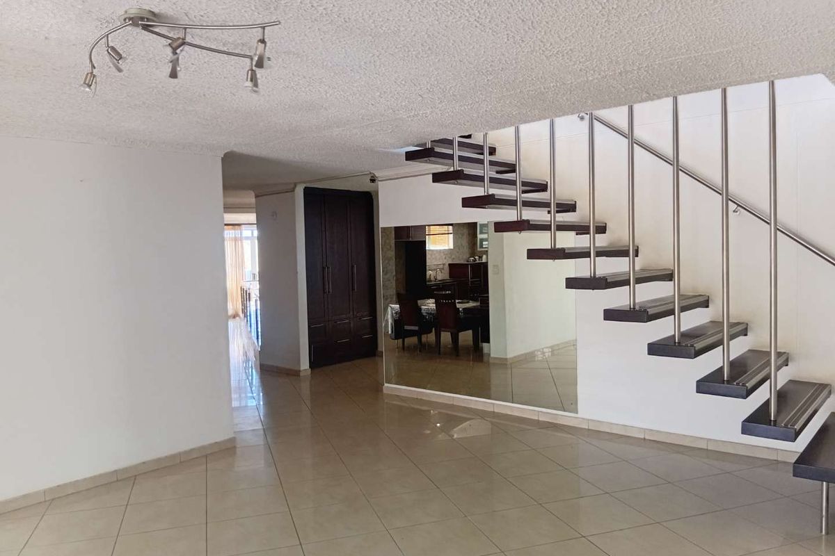 Spacious living area featuring a modern floating staircase with stainless steel balustrades, tiled flooring, and a mirrored wall accent.
