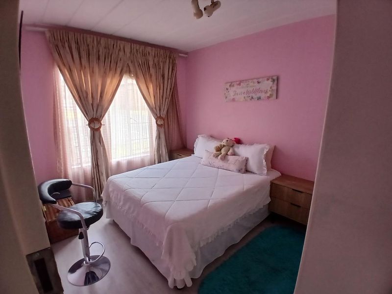 A cozy bedroom featuring pink walls, a window with curtains, and a ceiling light fixture.