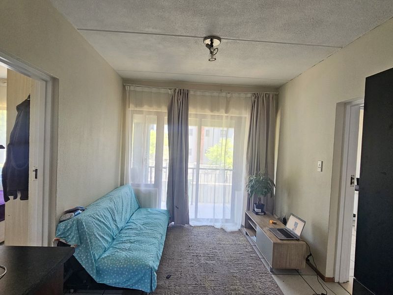 A living room featuring tiled flooring and a sliding glass door leading to a balcony, with access to adjacent rooms.