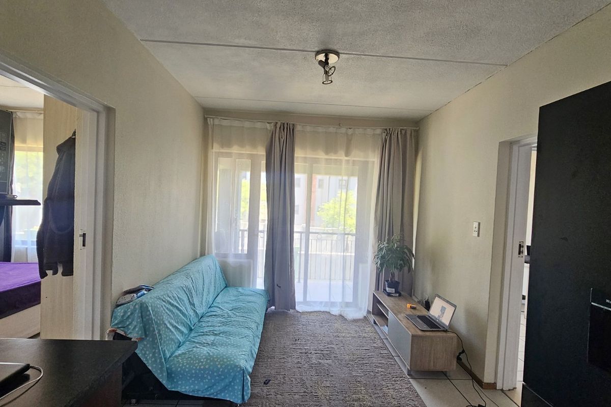 A living room featuring tiled flooring and a sliding glass door leading to a balcony, with access to adjacent rooms.