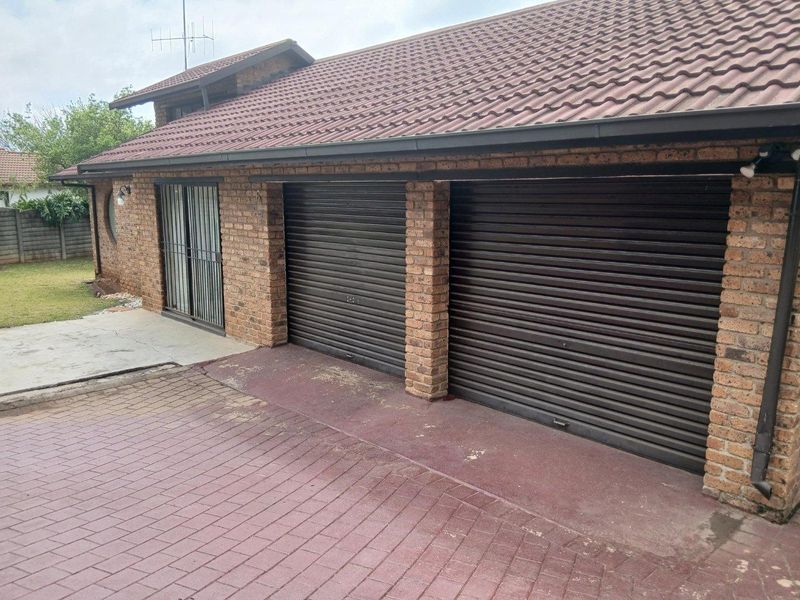 Exterior view of a double garage with roller doors, brick facade, and a paved driveway, featuring an adjacent sliding door entrance.