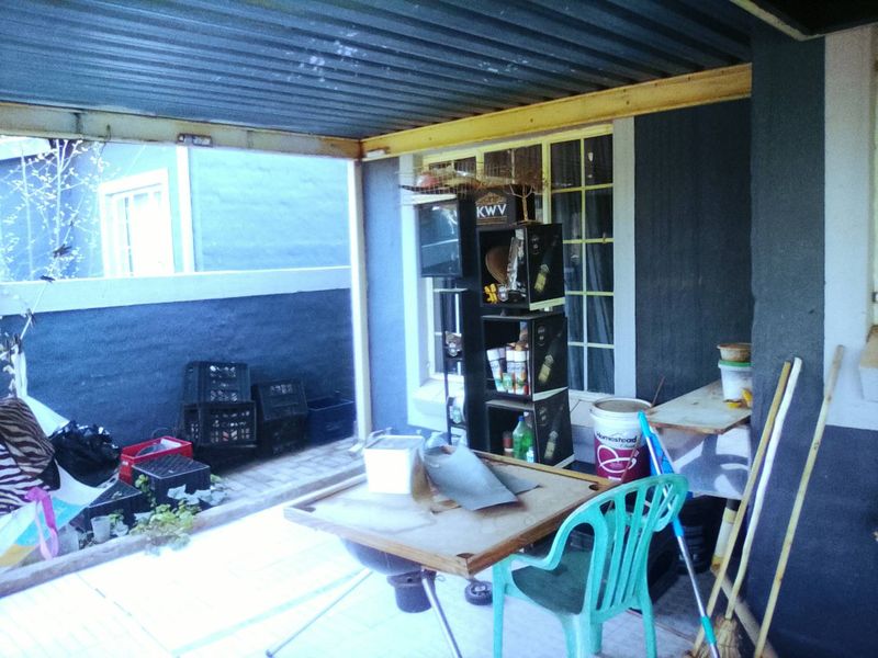 A covered outdoor patio area featuring a corrugated metal roof, paved flooring, and a boundary wall, offering potential for an improved entertainment space.