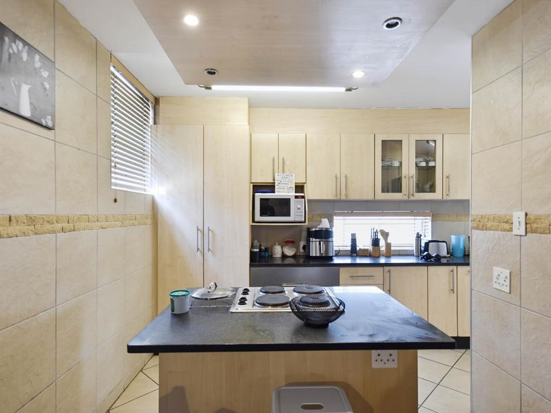 A functional kitchen featuring light wood cabinetry, a central island with an integrated electric hob, tiled walls, and ample storage space.