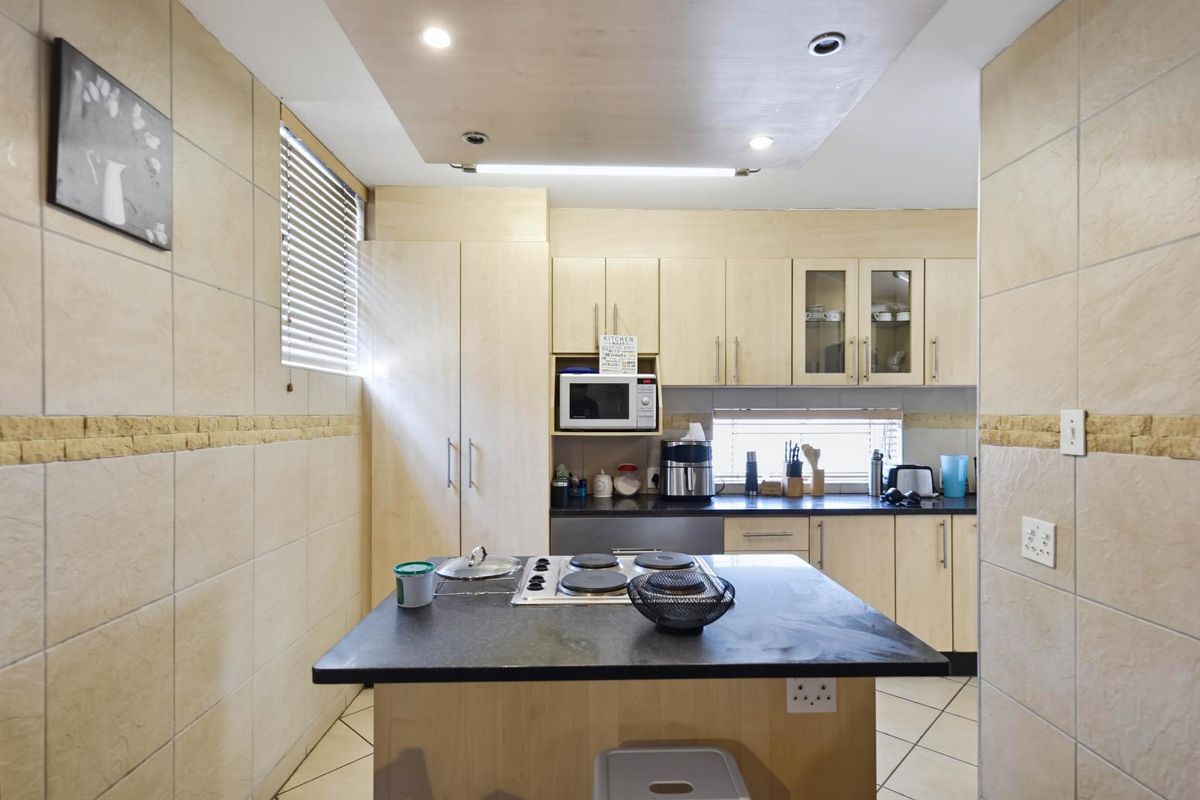 A functional kitchen featuring light wood cabinetry, a central island with an integrated electric hob, tiled walls, and ample storage space.