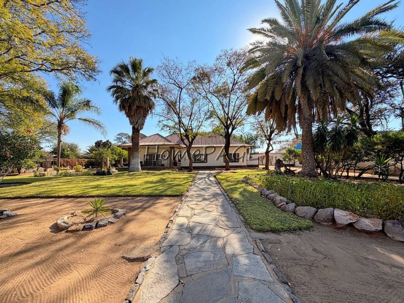 A well-maintained front garden featuring a stone paved walkway leading to the main house entrance, surrounded by mature trees and landscaped grounds.