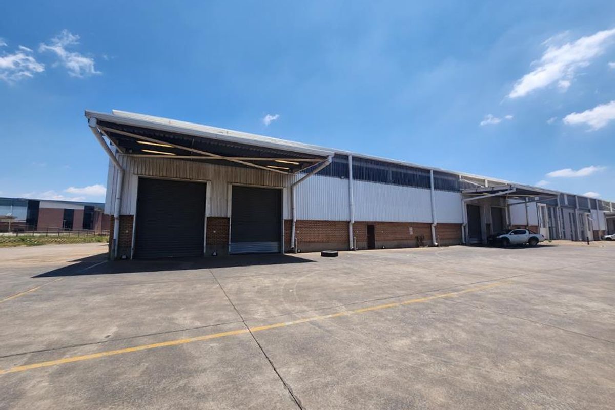 Industrial warehouse exterior featuring multiple roller shutter doors, covered loading bays, and a spacious concrete yard area.