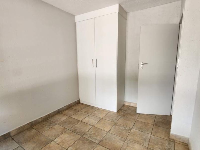 An empty bedroom featuring tiled flooring, a built-in wardrobe, and a standard interior door.