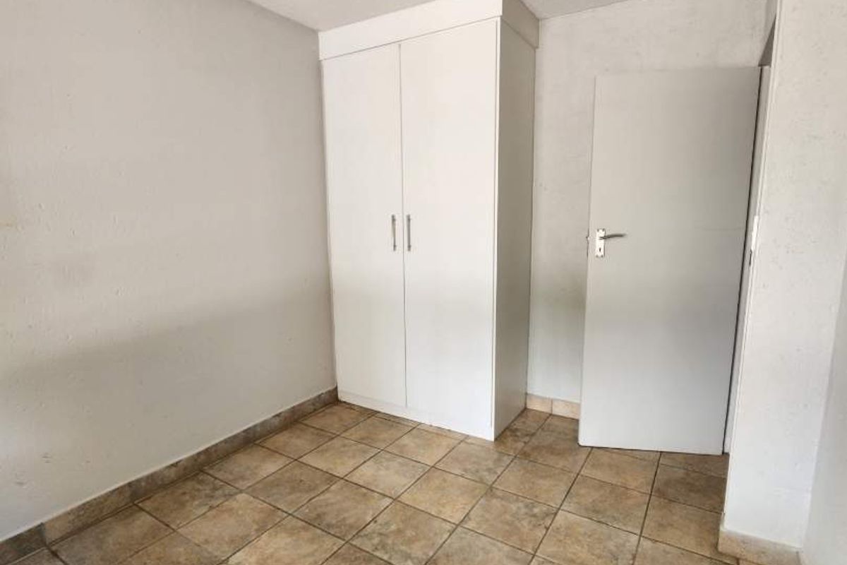 An empty bedroom featuring tiled flooring, a built-in wardrobe, and a standard interior door.