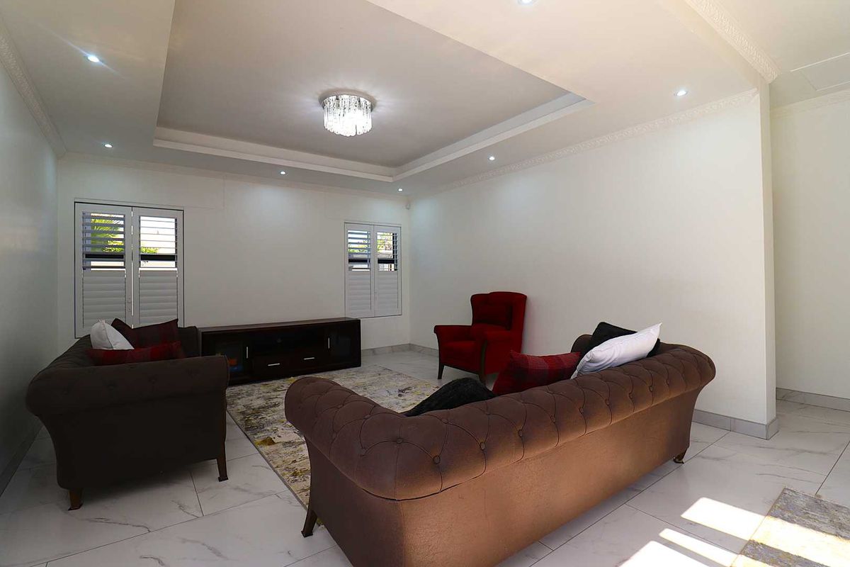 A bright and spacious living room featuring a tray ceiling with recessed lighting, modern tiled flooring, and white plantation shutters on the windows.