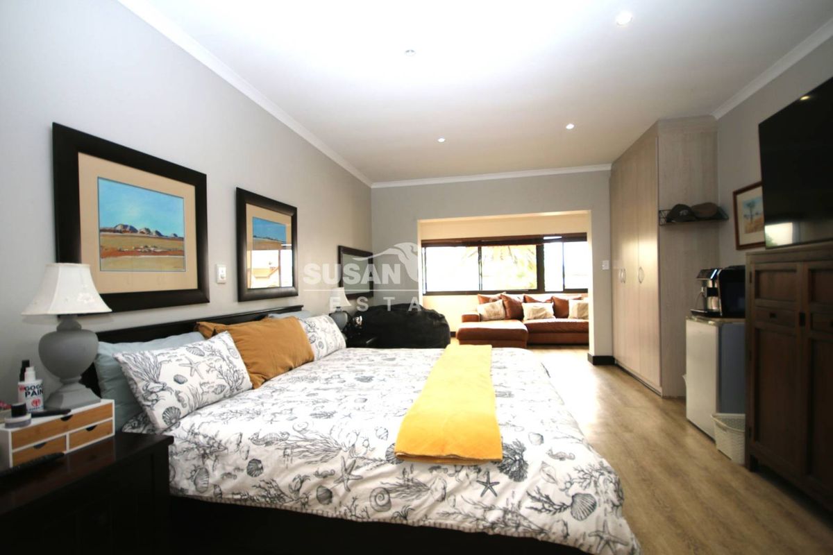 Spacious bedroom featuring built-in cupboards, recessed downlighting, and laminate flooring, with an adjoining seating area.