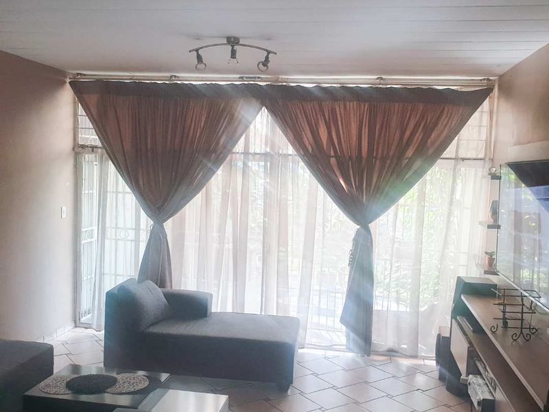 A living room featuring tiled flooring and a large sliding glass door with security gate, providing access to the outdoor area.
