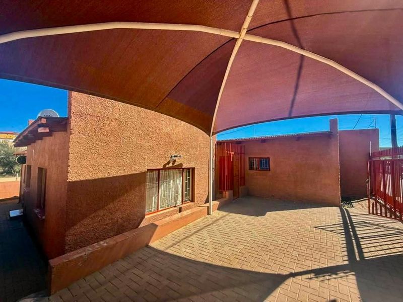 An outdoor paved patio area featuring a large shade sail, security gates, and security bars on the windows.