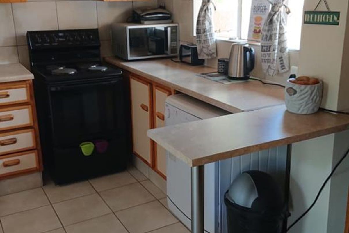 A functional kitchen featuring tiled flooring, laminate countertops, built-in cabinetry, and a breakfast bar, offering a practical layout for daily meal preparation.