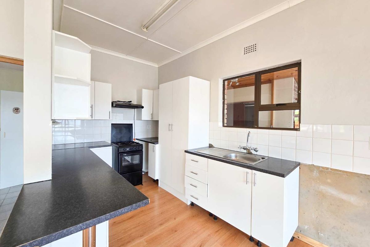 Functional kitchen featuring white cabinetry, dark laminate countertops, a freestanding stove, and a stainless steel sink with tiled splashbacks.