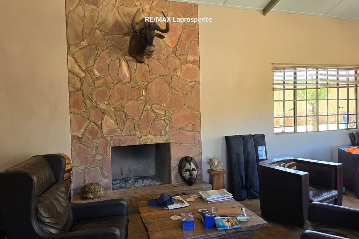 A living room featuring a prominent stone fireplace with a hearth and large windows with security bars.