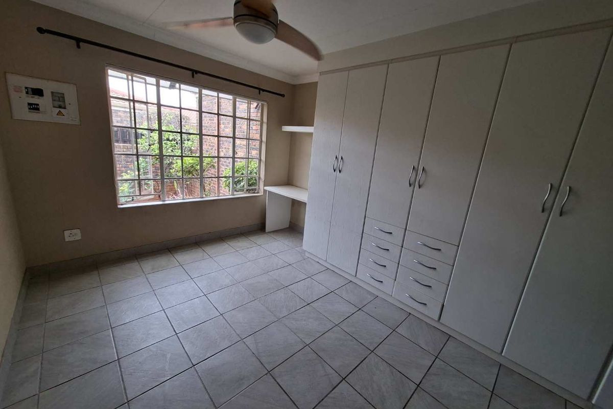 A spacious, empty bedroom featuring tiled flooring, extensive built-in cupboards, a built-in desk, and a ceiling fan.