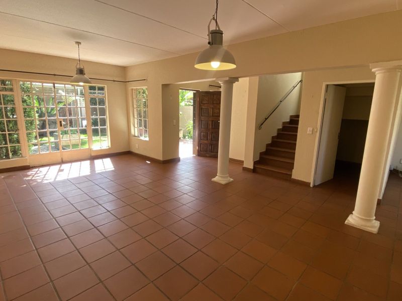 Spacious open-plan living area featuring terracotta floor tiles, structural columns, and direct access to the garden through classic french doors.