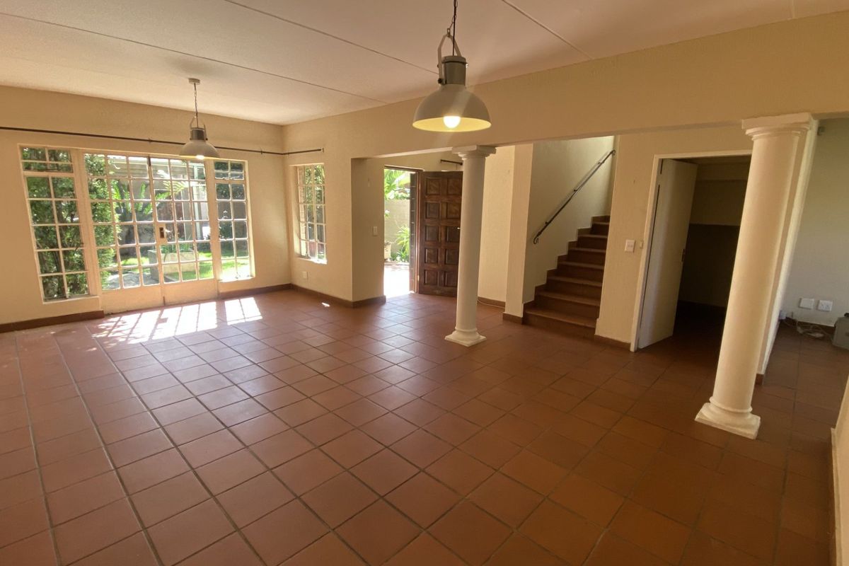 Spacious open-plan living area featuring terracotta floor tiles, structural columns, and direct access to the garden through classic french doors.