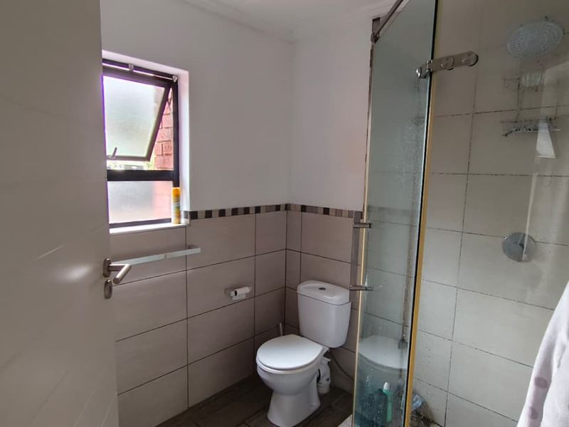 A functional bathroom featuring a glass-enclosed shower, toilet, and neutral wall tiling with a window for natural ventilation.
