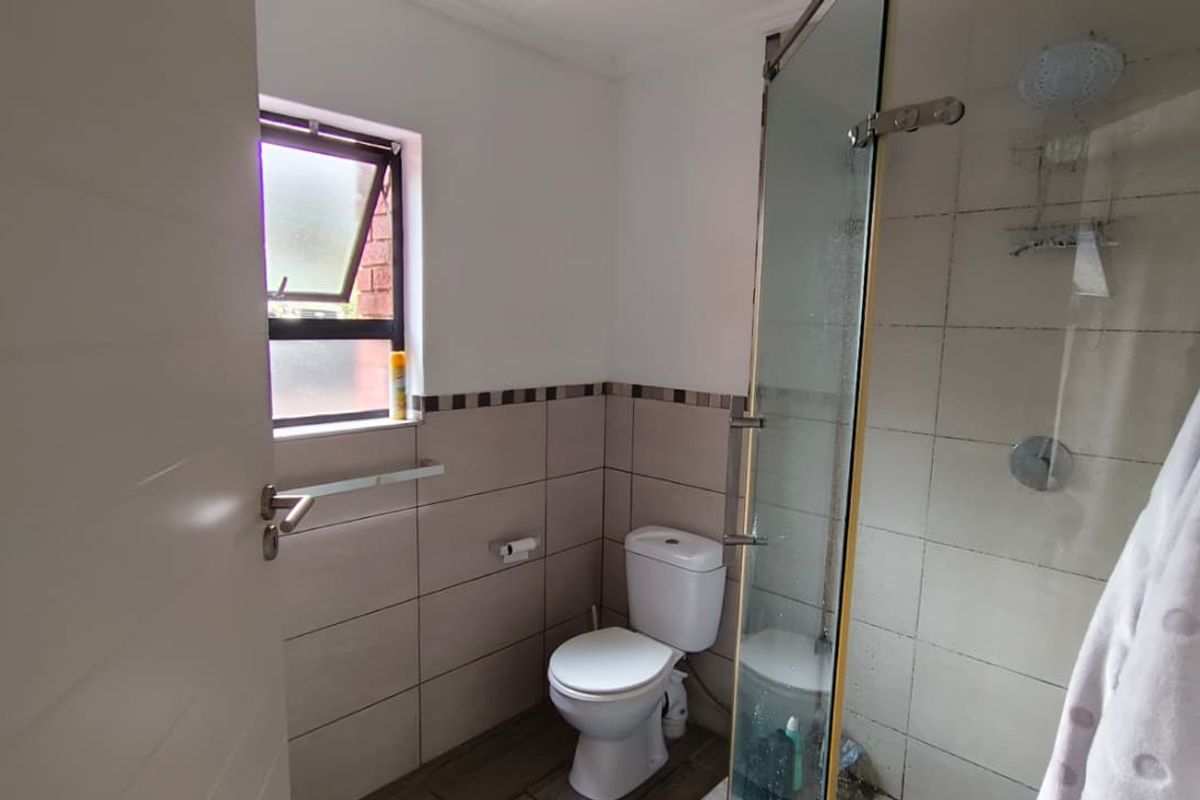 A functional bathroom featuring a glass-enclosed shower, toilet, and neutral wall tiling with a window for natural ventilation.