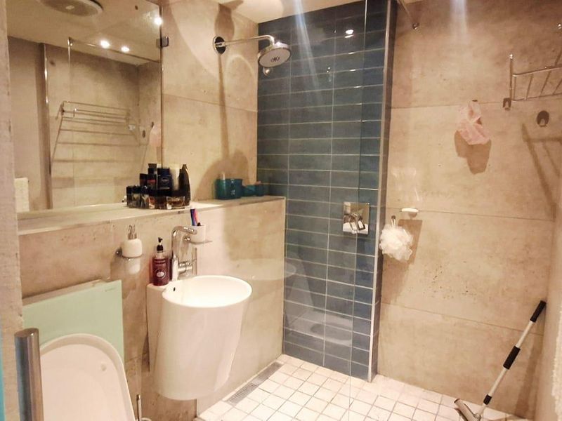 Modern bathroom featuring a walk-in shower with blue accent tiling, a wall-mounted basin, and a large integrated mirror.