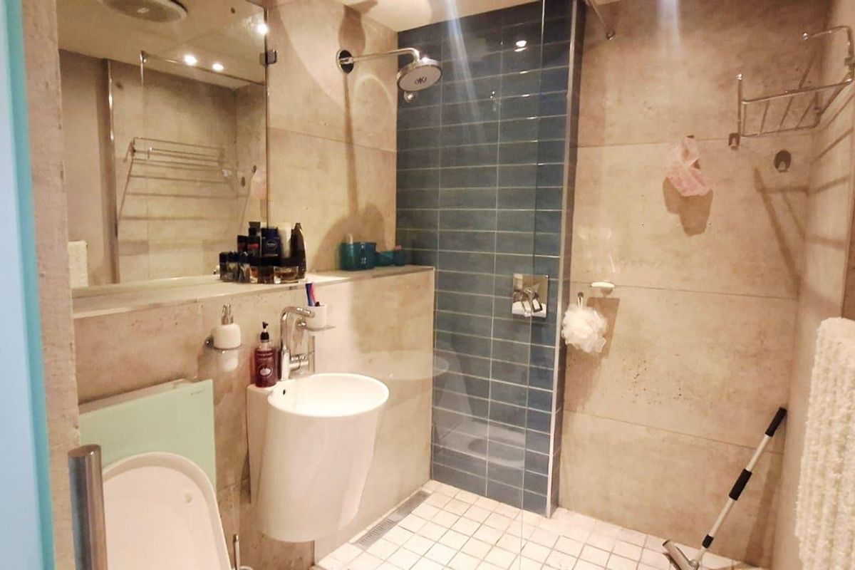 Modern bathroom featuring a walk-in shower with blue accent tiling, a wall-mounted basin, and a large integrated mirror.